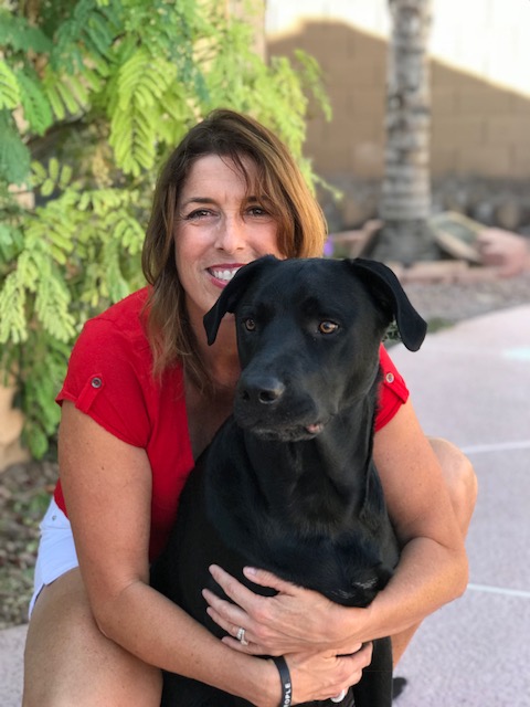 Natalie hugging a black dog outside.