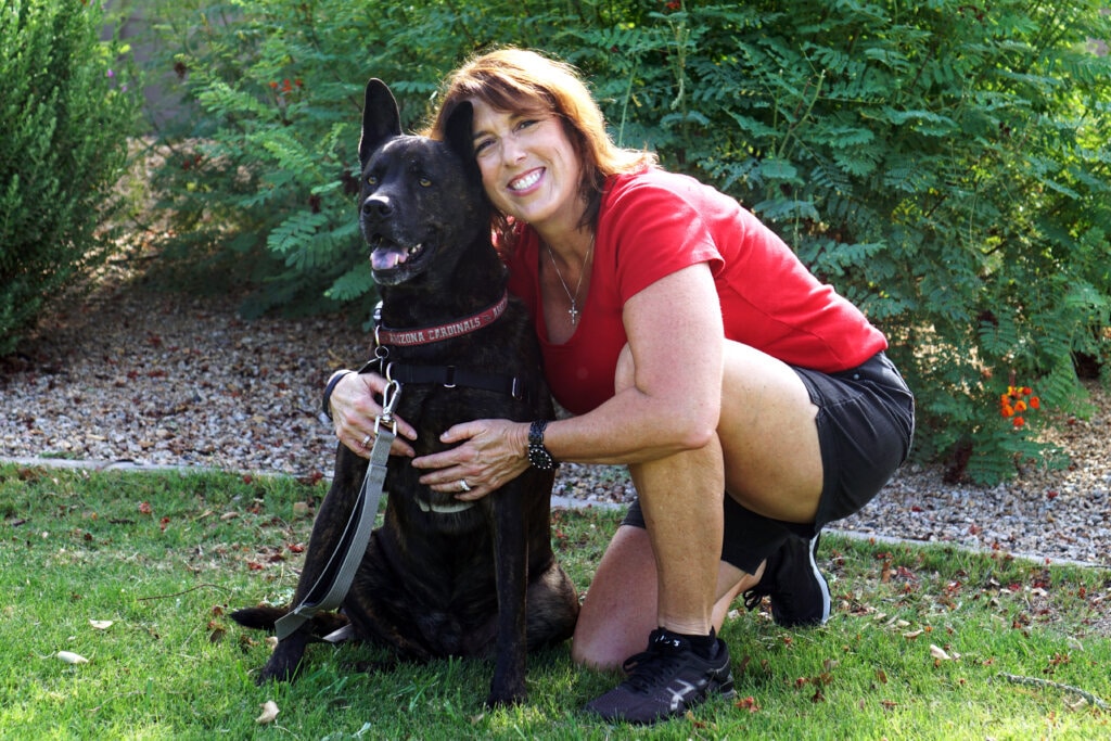 Natalie with her arm around a dog in front of a garden.