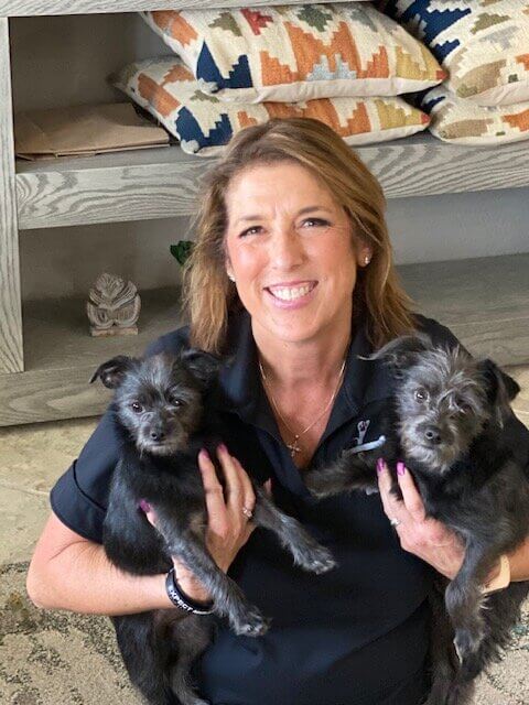 Natalie holding a small black dog in each arm.