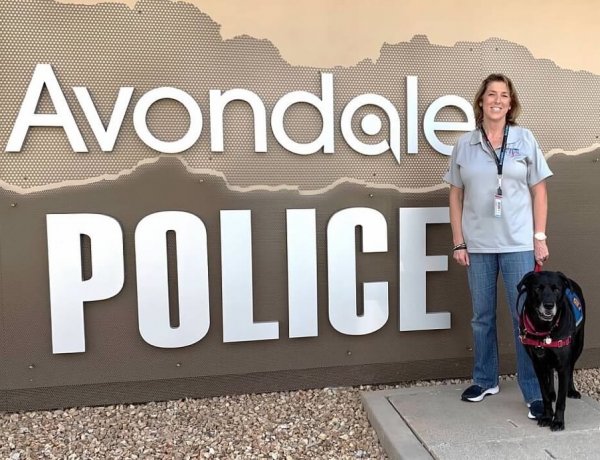 Natalie and a service vest wearing dog in front of an Avondale Police sign.